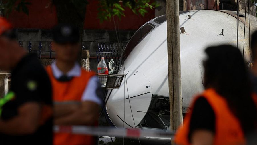 Orang-orang berdiri di dekat sisa-sisa pesawat Challenger 300 yang jatuh di dekat bandara San Fernando, di pinggiran Buenos Aires, Argentina, 18 Desember 2024. (REUTERS/Agustin Marcarian)