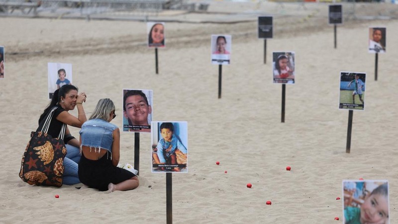 Seorang wanita berlari melewati 48 gambar anak-anak yang ditembak mati selama operasi polisi selama pemerintahan gubernur Rio de Janeiro Claudio Castro, oleh LSM Rio de Paz, di pantai Copacabana di Rio de Janeiro, Brasil, 18 Desember 2024. (REUTERS/Pilar Olivares)
