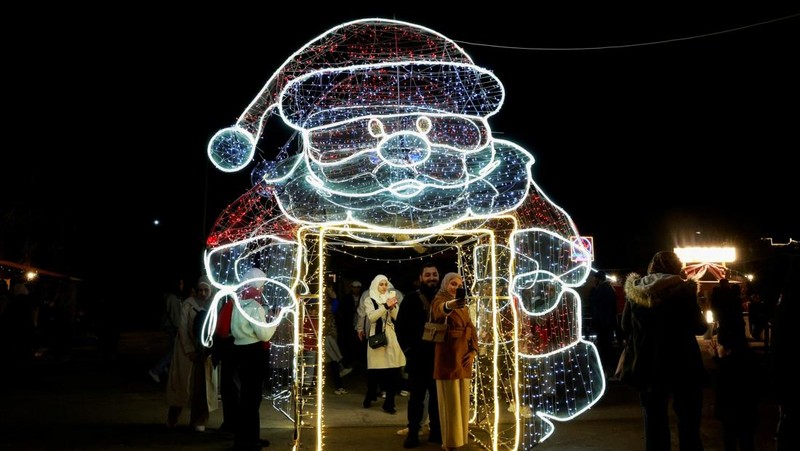 Para wanita memegang bendera yang diadopsi oleh penguasa baru Suriah, saat mereka berpose untuk difoto di dekat dekorasi Natal di Damaskus, setelah Bashar al-Assad digulingkan, di Damaskus, Suriah, 19 Desember 2024. (REUTERS/Ammar Awad)