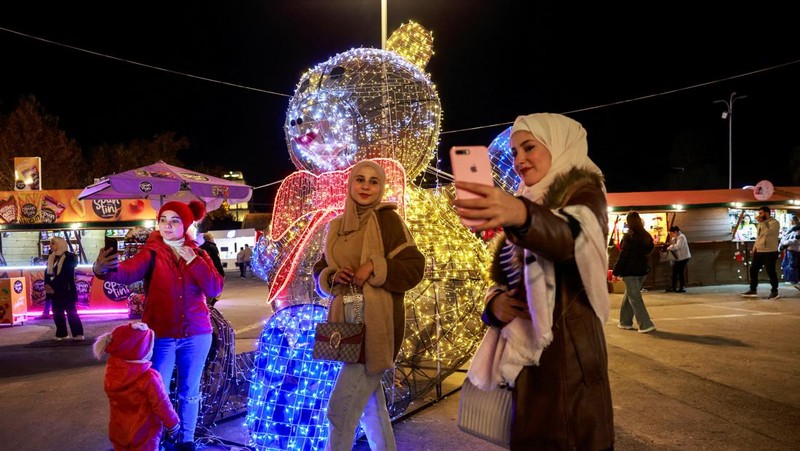 Para wanita memegang bendera yang diadopsi oleh penguasa baru Suriah, saat mereka berpose untuk difoto di dekat dekorasi Natal di Damaskus, setelah Bashar al-Assad digulingkan, di Damaskus, Suriah, 19 Desember 2024. (REUTERS/Ammar Awad)