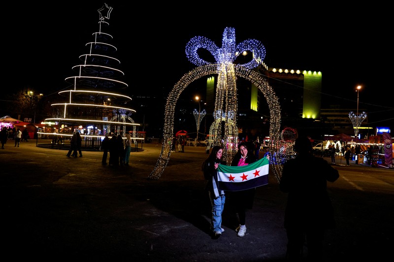 Para wanita memegang bendera yang diadopsi oleh penguasa baru Suriah, saat mereka berpose untuk difoto di dekat dekorasi Natal di Damaskus, setelah Bashar al-Assad digulingkan, di Damaskus, Suriah, 19 Desember 2024. Para wanita memegang bendera yang diadopsi oleh penguasa baru Suriah, saat mereka berpose untuk difoto di dekat dekorasi Natal di Damaskus, setelah Bashar al-Assad digulingkan, di Damaskus, Suriah, 19 Desember 2024. (REUTERS/Ammar Awad)