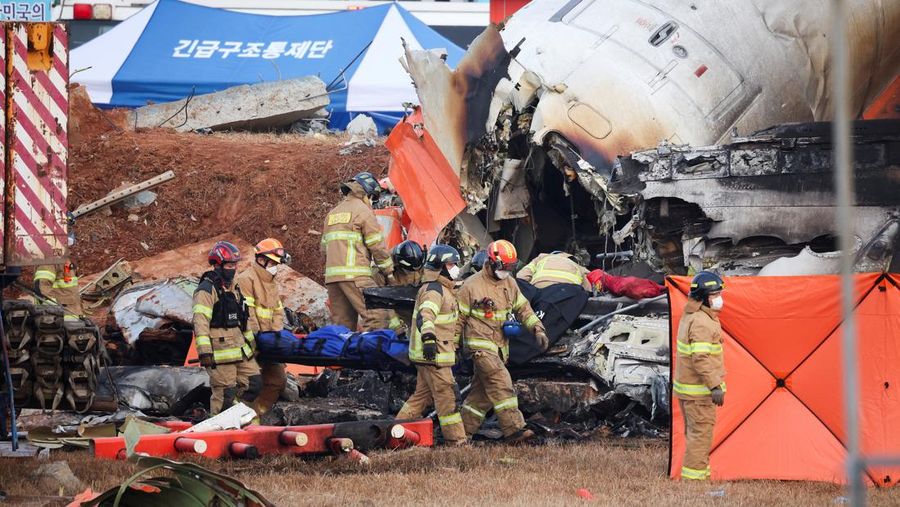Petugas pemadam kebakaran membawa jenazah penumpang dari reruntuhan pesawat yang jatuh setelah keluar landasan di Bandara Internasional Muan, di Muan, Korea Selatan, 29 Desember 2024. (REUTERS/Kim Hong-Ji)