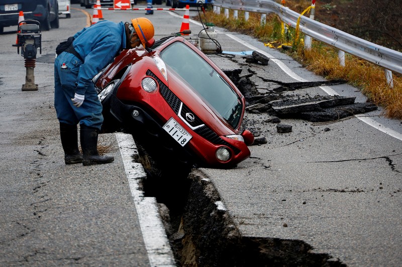 YEAR-END/2024-PHOTOS-BEST A worker looks at a car stuck on a broken road in the aftermath of an earthquake, near Anamizu, Japan, January 3, 2024. REUTERS/Kim Kyung-Hoon SEARCH
