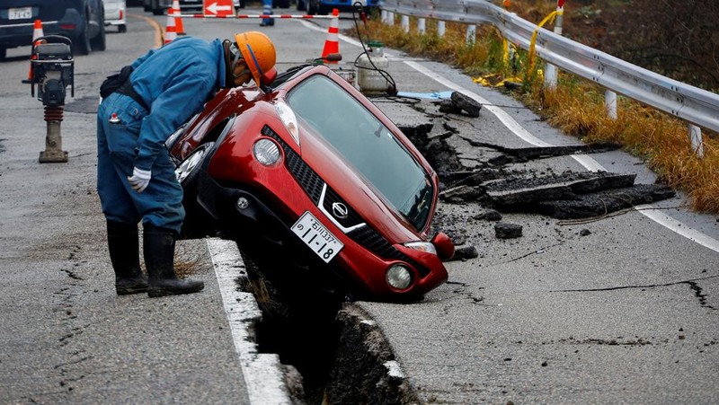 A worker looks at a car stuck on a broken road in the aftermath of an earthquake, near Anamizu, Japan, January 3, 2024. REUTERS/Kim Kyung-Hoon          SEARCH 