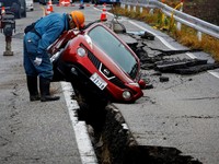 A worker looks at a car stuck on a broken road in the aftermath of an earthquake, near Anamizu, Japan, January 3, 2024. REUTERS/Kim Kyung-Hoon