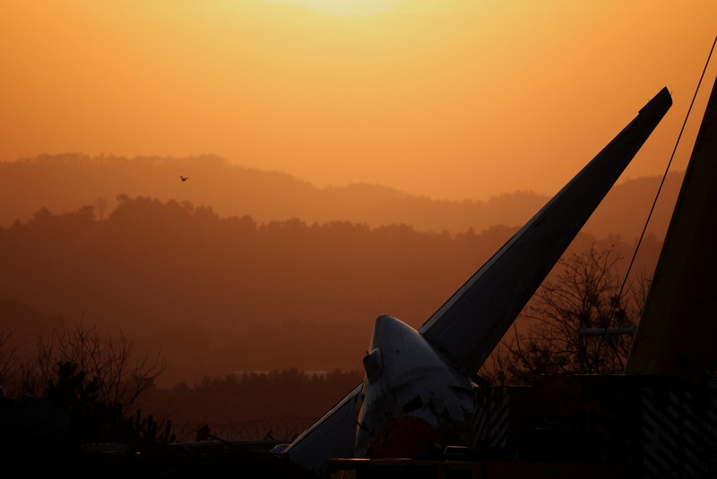 A bird flies by as the sun rises behind the aircraft that crashed after it went off the runway, at Muan International Airport, in Muan, South Korea, December 31, 2024. REUTERS/Kim Hong-Ji