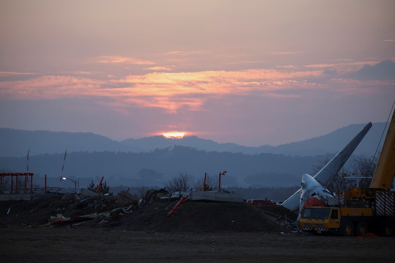 SOUTHKOREA-CRASH/ A bird flies by as the sun rises behind the aircraft that crashed after it went off the runway, at Muan International Airport, in Muan, South Korea, December 31, 2024. REUTERS/Kim Hong-Ji