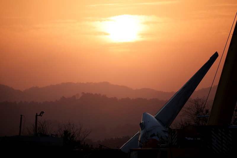 SOUTHKOREA-CRASH/ A bird flies by as the sun rises behind the aircraft that crashed after it went off the runway, at Muan International Airport, in Muan, South Korea, December 31, 2024. REUTERS/Kim Hong-Ji