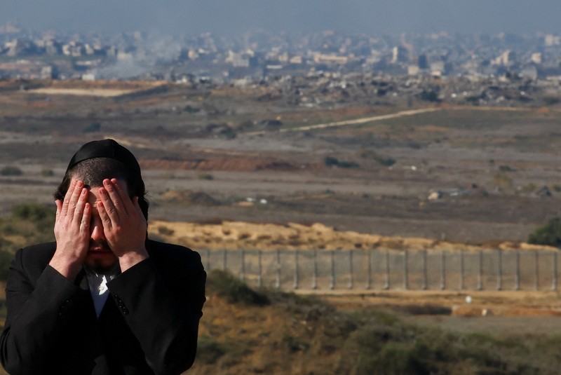 Seorang pria Yahudi Ultra-Ortodoks menyeka wajahnya, dengan latar belakang Gaza utara saat militer Israel melakukan operasi di dalam Jalur Gaza, di tengah konflik yang sedang berlangsung antara Israel dan Hamas, seperti yang terlihat dari Israel selatan, 1 Januari 2025. (REUTERS/Kai Pfaffenbach)