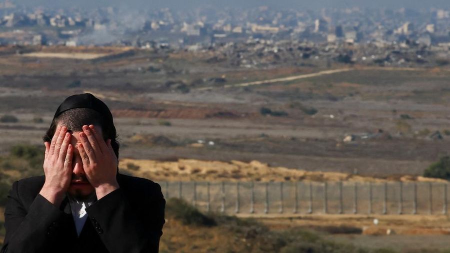 Seorang pria Yahudi Ultra-Ortodoks menyeka wajahnya, dengan latar belakang Gaza utara saat militer Israel melakukan operasi di dalam Jalur Gaza, di tengah konflik yang sedang berlangsung antara Israel dan Hamas, seperti yang terlihat dari Israel selatan, 1 Januari 2025. (REUTERS/Kai Pfaffenbach)