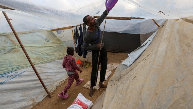 Warga Palestina Tayseer Obaid, bersama keluarganya duduk di dalam lubang bawah tanah yang digalinya untuk melindungi dari serangan Israel di perkemahan pengungsi Deir Al-Balah, Jalur Gaza bagian tengah, Senin (6/1/2025). (REUTERS/Ramadan Abed)