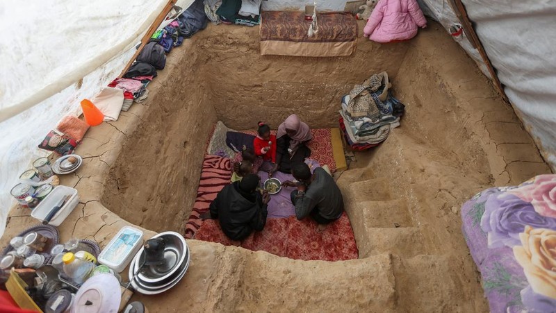 Warga Palestina Tayseer Obaid, bersama keluarganya duduk di dalam lubang bawah tanah yang digalinya untuk melindungi dari serangan Israel di perkemahan pengungsi Deir Al-Balah, Jalur Gaza bagian tengah, Senin (6/1/2025). (REUTERS/Ramadan Abed)