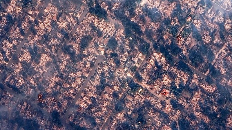 Seorang yang membawa bendera berjalan menjauh dari rumah yang terbakar saat angin kencang yang memicu kebakaran hutan yang dahsyat di wilayah Los Angeles memaksa orang-orang untuk mengungsi, di Kebakaran Eaton di Altadena, California, AS, 8 Januari 2025. (REUTERS/David Swanson)