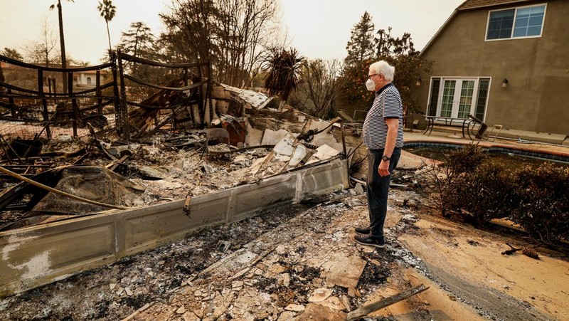 Seorang yang membawa bendera berjalan menjauh dari rumah yang terbakar saat angin kencang yang memicu kebakaran hutan yang dahsyat di wilayah Los Angeles memaksa orang-orang untuk mengungsi, di Kebakaran Eaton di Altadena, California, AS, 8 Januari 2025. (REUTERS/David Swanson)