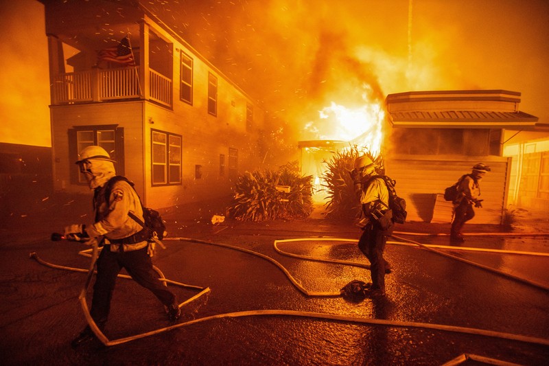 Seorang yang membawa bendera berjalan menjauh dari rumah yang terbakar saat angin kencang yang memicu kebakaran hutan yang dahsyat di wilayah Los Angeles memaksa orang-orang untuk mengungsi, di Kebakaran Eaton di Altadena, California, AS, 8 Januari 2025. (REUTERS/David Swanson)