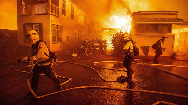 Seorang yang membawa bendera berjalan menjauh dari rumah yang terbakar saat angin kencang yang memicu kebakaran hutan yang dahsyat di wilayah Los Angeles memaksa orang-orang untuk mengungsi, di Kebakaran Eaton di Altadena, California, AS, 8 Januari 2025. (REUTERS/David Swanson)