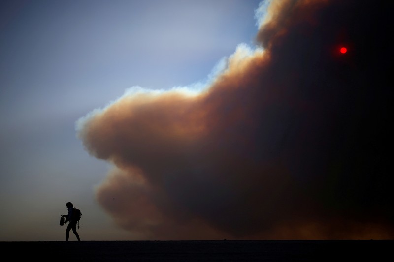 Seorang yang membawa bendera berjalan menjauh dari rumah yang terbakar saat angin kencang yang memicu kebakaran hutan yang dahsyat di wilayah Los Angeles memaksa orang-orang untuk mengungsi, di Kebakaran Eaton di Altadena, California, AS, 8 Januari 2025. (REUTERS/David Swanson) Seorang yang membawa bendera berjalan menjauh dari rumah yang terbakar saat angin kencang yang memicu kebakaran hutan yang dahsyat di wilayah Los Angeles memaksa orang-orang untuk mengungsi, di Kebakaran Eaton di Altadena, California, AS, 8 Januari 2025. (REUTERS/David Swanson)