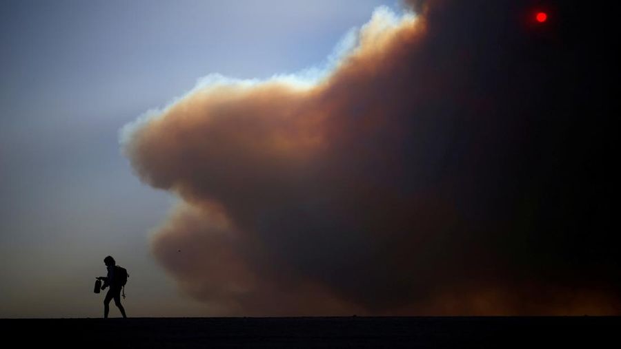 Seorang yang membawa bendera berjalan menjauh dari rumah yang terbakar saat angin kencang yang memicu kebakaran hutan yang dahsyat di wilayah Los Angeles memaksa orang-orang untuk mengungsi, di Kebakaran Eaton di Altadena, California, AS, 8 Januari 2025. (REUTERS/David Swanson)