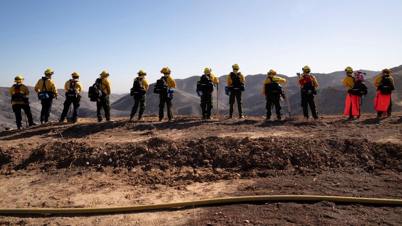 Petugas pemadam kebakaran dari Meksiko beristirahat sambil mendaki ke tujuan mereka untuk memotong garis penahanan di daerah Tarzana selama Kebakaran Palisades di Los Angeles, California, AS, 13 Januari 2025. (REUTERS/David Ryder)