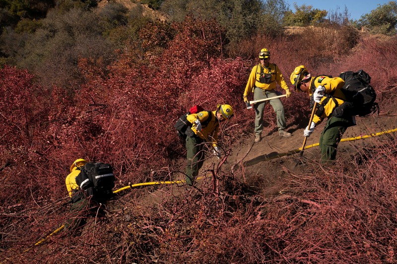 Petugas pemadam kebakaran dari Meksiko beristirahat sambil mendaki ke tujuan mereka untuk memotong garis penahanan di daerah Tarzana selama Kebakaran Palisades di Los Angeles, California, AS, 13 Januari 2025. (REUTERS/David Ryder)
