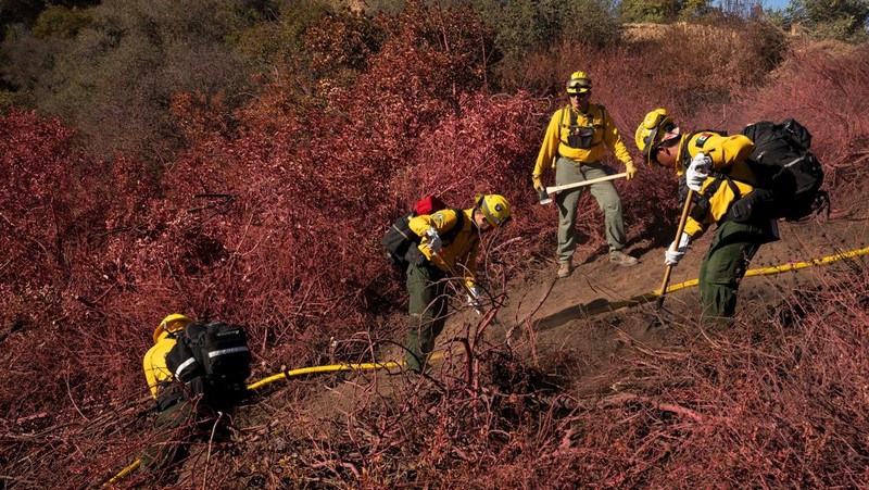 Petugas pemadam kebakaran dari Meksiko beristirahat sambil mendaki ke tujuan mereka untuk memotong garis penahanan di daerah Tarzana selama Kebakaran Palisades di Los Angeles, California, AS, 13 Januari 2025. (REUTERS/David Ryder)