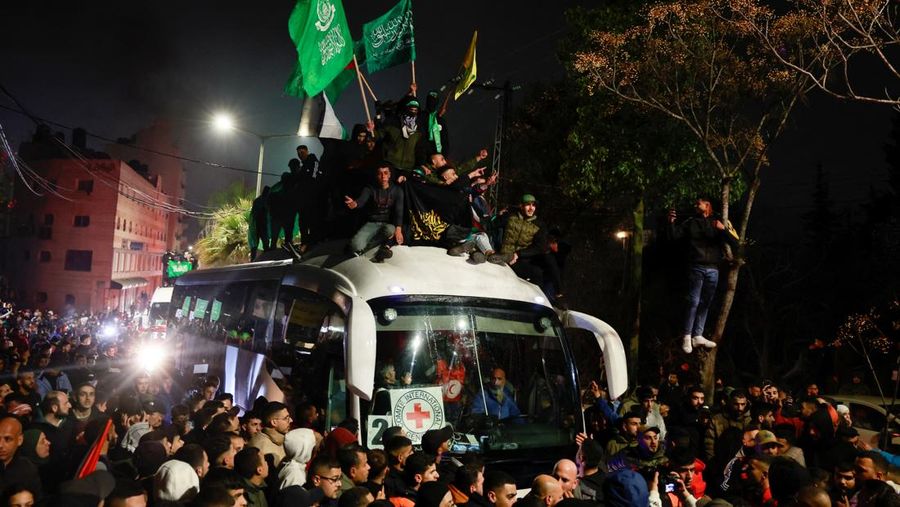 Orang-orang yang membawa bendera berdiri di atas bus saat mereka bereaksi terhadap kedatangan bus yang membawa warga Palestina yang dibebaskan dari penjara Israel sebagai bagian dari pertukaran sandera-tahanan dan kesepakatan gencatan senjata antara Hamas dan Israel, di Ramallah di Tepi Barat yang diduduki Israel. 20 Januari 2025. (REUTERS/Mussa Qawasma)