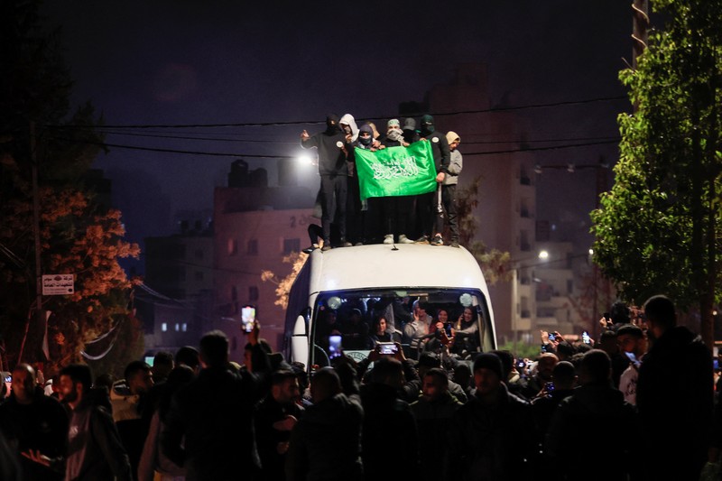 Orang-orang yang membawa bendera berdiri di atas bus saat mereka bereaksi terhadap kedatangan bus yang membawa warga Palestina yang dibebaskan dari penjara Israel sebagai bagian dari pertukaran sandera-tahanan dan kesepakatan gencatan senjata antara Hamas dan Israel, di Ramallah di Tepi Barat yang diduduki Israel. 20 Januari 2025. (REUTERS/Mussa Qawasma)