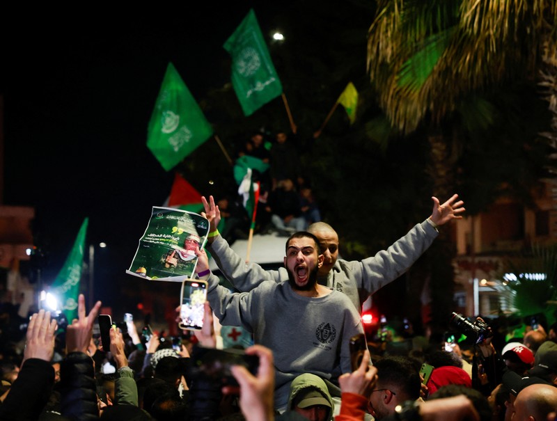 Orang-orang yang membawa bendera berdiri di atas bus saat mereka bereaksi terhadap kedatangan bus yang membawa warga Palestina yang dibebaskan dari penjara Israel sebagai bagian dari pertukaran sandera-tahanan dan kesepakatan gencatan senjata antara Hamas dan Israel, di Ramallah di Tepi Barat yang diduduki Israel. 20 Januari 2025. (REUTERS/Mussa Qawasma)
