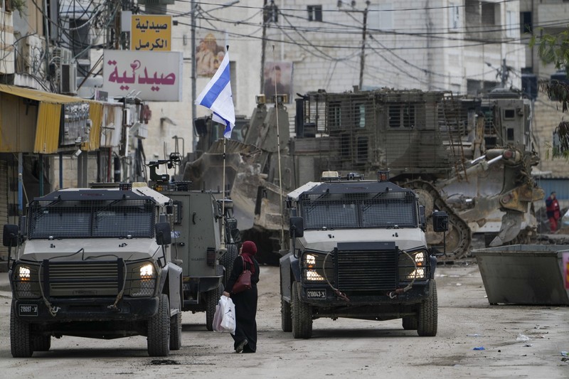 Israel Palestinians Israeli military vehicles guard a road where a military bulldozer operates in the West Bank refugee camp of Jenin Wednesday, Jan. 22, 2025. (AP Photo/Majdi Mohammed)