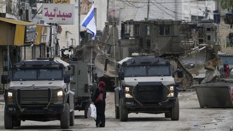 Israeli military vehicles guard a road where a military bulldozer operates in the West Bank refugee camp of Jenin Wednesday, Jan. 22, 2025. (AP Photo/Majdi Mohammed)