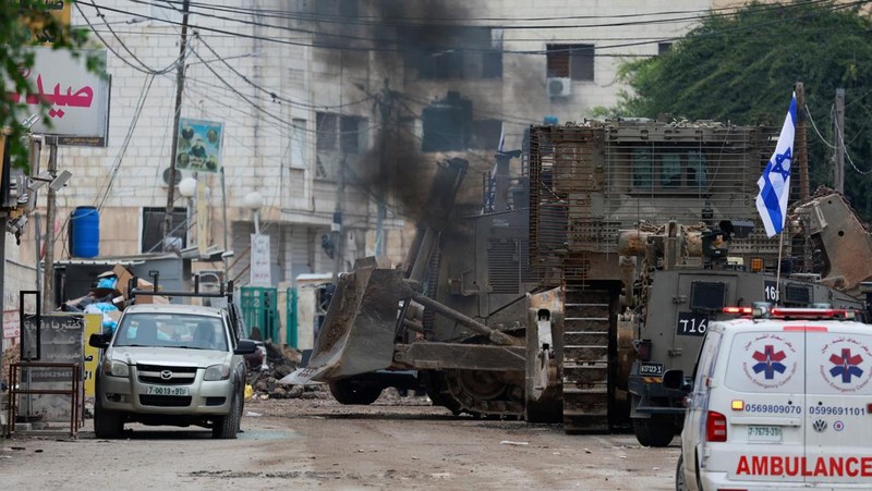 Israeli military vehicles guard a road where a military bulldozer operates in the West Bank refugee camp of Jenin Wednesday, Jan. 22, 2025. (AP Photo/Majdi Mohammed)