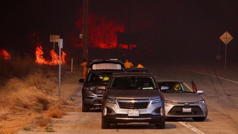 Anggota media bekerja saat asap dan api mengepul saat petugas pemadam kebakaran berjuang memadamkan Kebakaran Hughes di dekat Danau Castaic, utara Santa Clarita, California, AS, 22 Januari 2025. (REUTERS/David Swanson)