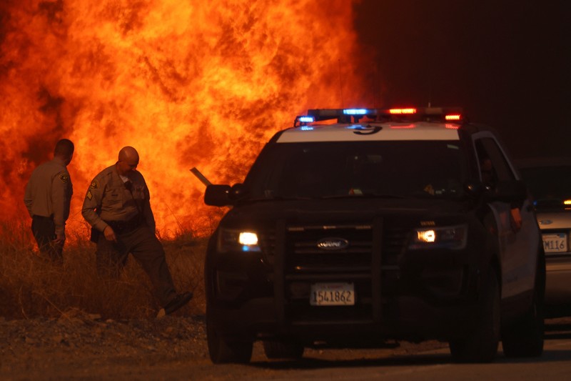 Anggota media bekerja saat asap dan api mengepul saat petugas pemadam kebakaran berjuang memadamkan Kebakaran Hughes di dekat Danau Castaic, utara Santa Clarita, California, AS, 22 Januari 2025. (REUTERS/David Swanson)