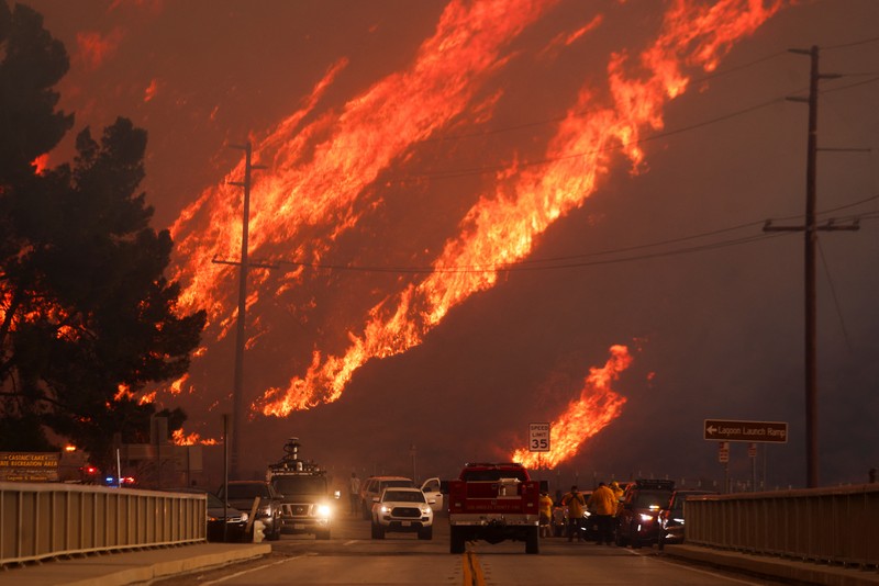 Anggota media bekerja saat asap dan api mengepul saat petugas pemadam kebakaran berjuang memadamkan Kebakaran Hughes di dekat Danau Castaic, utara Santa Clarita, California, AS, 22 Januari 2025. Anggota media bekerja saat asap dan api mengepul saat petugas pemadam kebakaran berjuang memadamkan Kebakaran Hughes di dekat Danau Castaic, utara Santa Clarita, California, AS, 22 Januari 2025. (REUTERS/David Swanson)