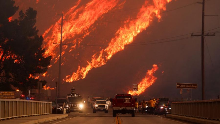 Anggota media bekerja saat asap dan api mengepul saat petugas pemadam kebakaran berjuang memadamkan Kebakaran Hughes di dekat Danau Castaic, utara Santa Clarita, California, AS, 22 Januari 2025. (REUTERS/David Swanson)