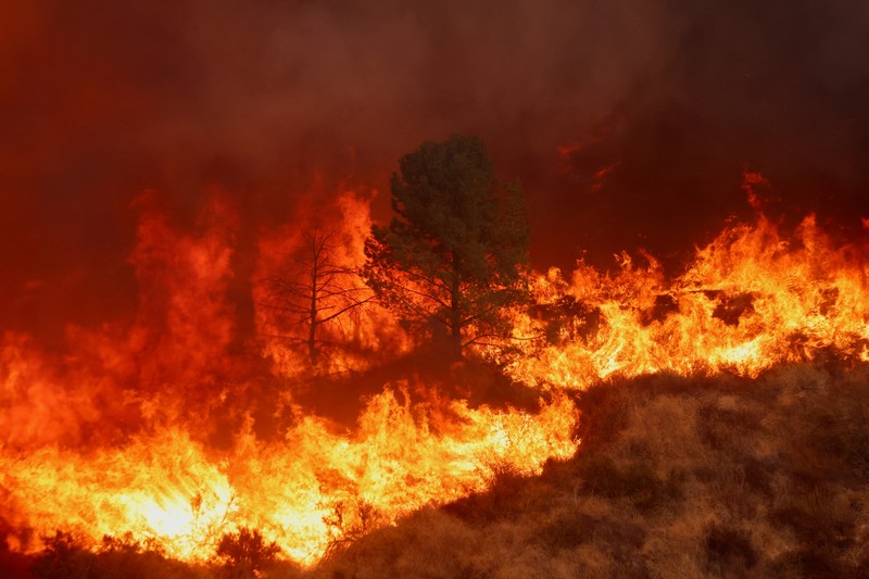 Anggota media bekerja saat asap dan api mengepul saat petugas pemadam kebakaran berjuang memadamkan Kebakaran Hughes di dekat Danau Castaic, utara Santa Clarita, California, AS, 22 Januari 2025. (REUTERS/David Swanson)