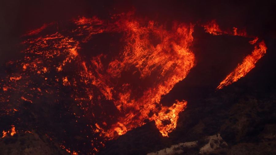 Anggota media bekerja saat asap dan api mengepul saat petugas pemadam kebakaran berjuang memadamkan Kebakaran Hughes di dekat Danau Castaic, utara Santa Clarita, California, AS, 22 Januari 2025. (REUTERS/David Swanson)