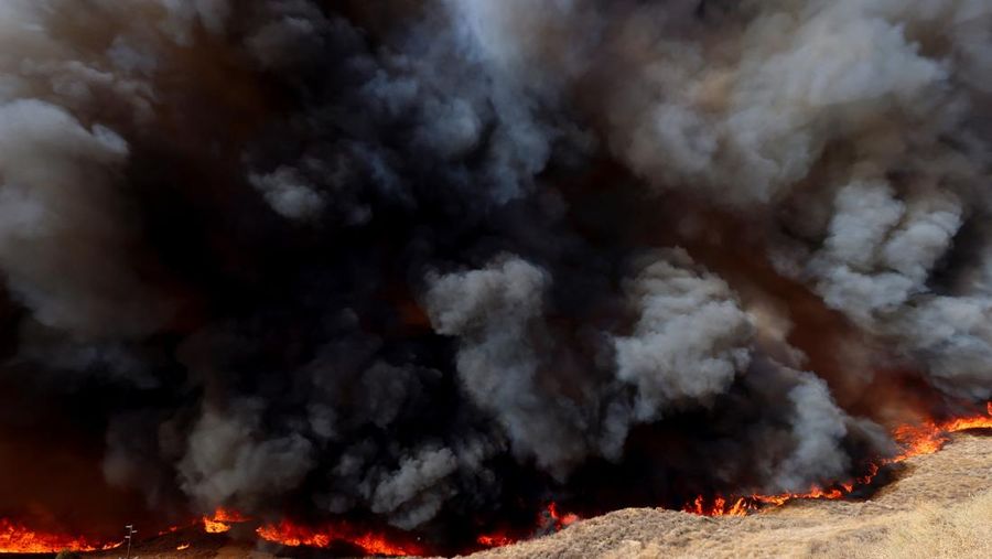 Anggota media bekerja saat asap dan api mengepul saat petugas pemadam kebakaran berjuang memadamkan Kebakaran Hughes di dekat Danau Castaic, utara Santa Clarita, California, AS, 22 Januari 2025. (REUTERS/David Swanson)