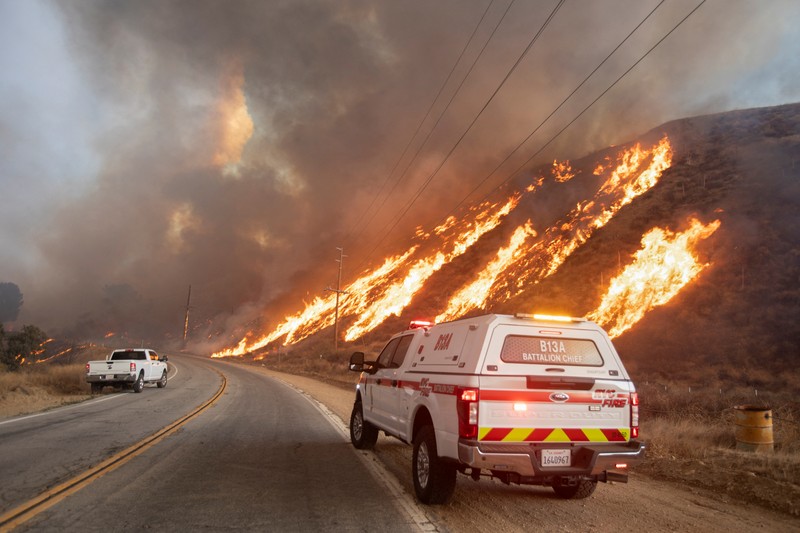 Seorang petugas pemadam kebakaran membawa obor tetes saat ia menyalakan api unggun untuk memadamkan Kebakaran Hughes yang membakar sepanjang lereng bukit di Castaic, California, Rabu, 22 Januari 2025. (AP Photo/Jae C. Hong)