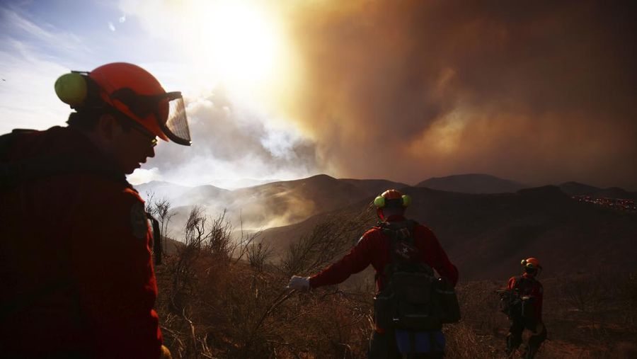 Anggota media bekerja saat asap dan api mengepul saat petugas pemadam kebakaran berjuang memadamkan Kebakaran Hughes di dekat Danau Castaic, utara Santa Clarita, California, AS, 22 Januari 2025. (REUTERS/David Swanson)