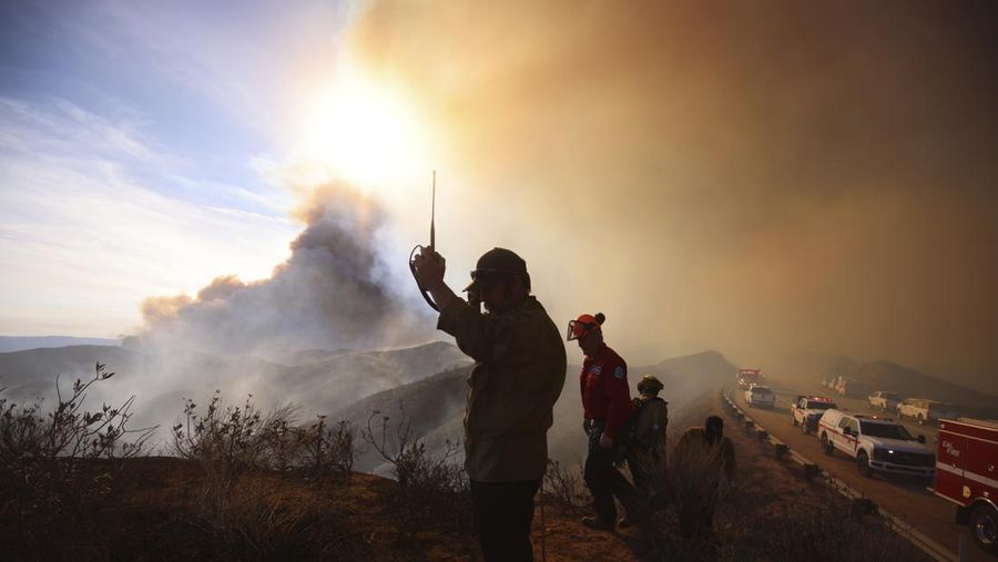 Anggota media bekerja saat asap dan api mengepul saat petugas pemadam kebakaran berjuang memadamkan Kebakaran Hughes di dekat Danau Castaic, utara Santa Clarita, California, AS, 22 Januari 2025. (REUTERS/David Swanson)