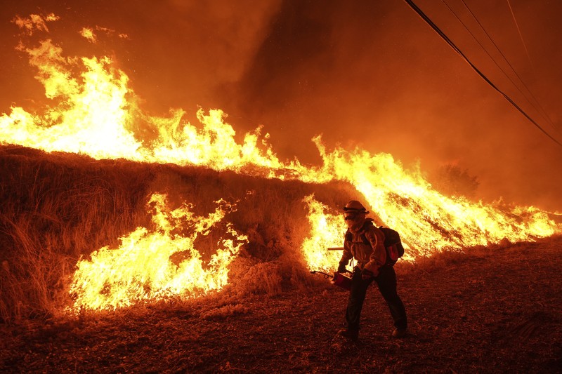 Seorang petugas pemadam kebakaran membawa obor tetes saat ia menyalakan api unggun untuk memadamkan Kebakaran Hughes yang membakar sepanjang lereng bukit di Castaic, California, Rabu, 22 Januari 2025. (AP Photo/Jae C. Hong)