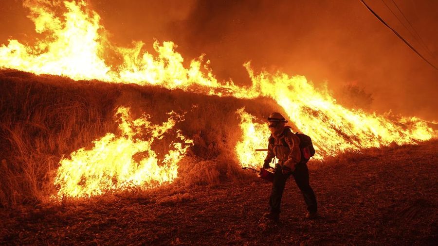 Seorang petugas pemadam kebakaran membawa obor tetes saat ia menyalakan api unggun untuk memadamkan Kebakaran Hughes yang membakar sepanjang lereng bukit di Castaic, California, Rabu, 22 Januari 2025. (AP Photo/Jae C. Hong)