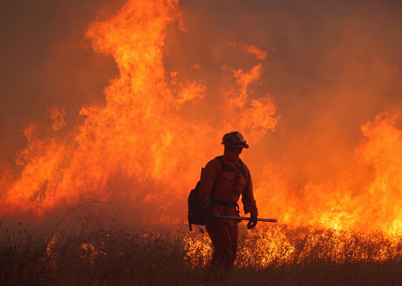 Seorang petugas pemadam kebakaran membawa obor tetes saat ia menyalakan api unggun untuk memadamkan Kebakaran Hughes yang membakar sepanjang lereng bukit di Castaic, California, Rabu, 22 Januari 2025. (AP Photo/Jae C. Hong)