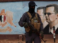 Seorang anggota bekas kelompok pemberontak Hayat Tahrir al-Sham berdiri berjaga di dekat gambar Bashar al-Assad dari Suriah di markas divisi keempat di Damaskus, Suriah, 23 Januari 2025. (REUTERS/Yamam Al Shaar)