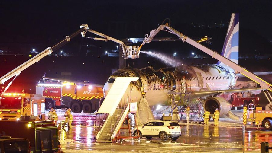 Petugas pemadam kebakaran berupaya memadamkan api pada pesawat Air Busan di Bandara Internasional Gimhae di Busan, Korea Selatan, Selasa (28/1/2025). (Son Hyung-joo/Yonhap via AP)