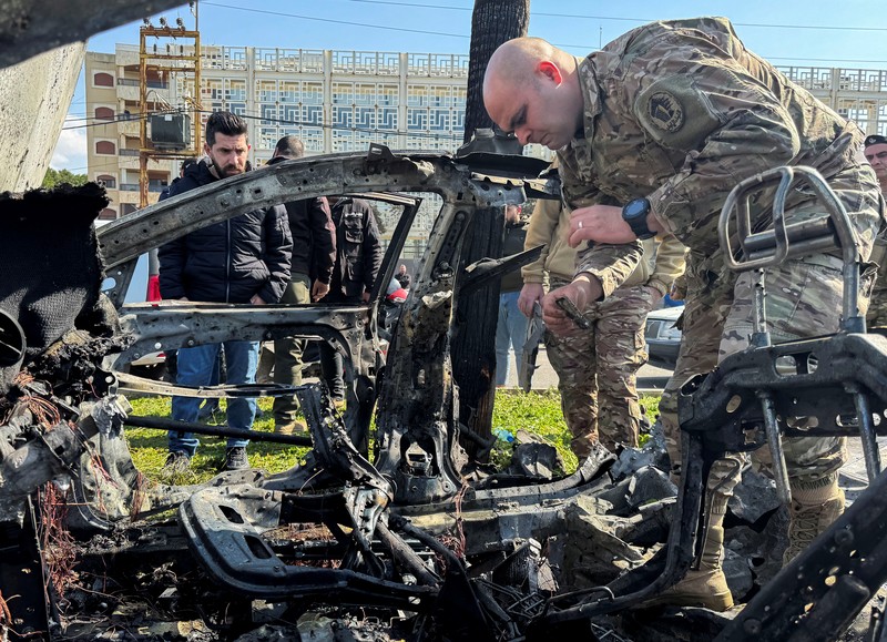 Warga dan pasukan keamanan berkumpul di dekat mobil yang rusak setelah serangan Israel, menurut sumber keamanan, di kota pelabuhan selatan Sidon, Lebanon, 17 Februari 2025. (REUTERS/ALI HANKIR)
