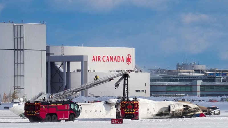 Petugas pemadam kebakaran Bandara Internasional Pearson bekerja pada pesawat Delta Air Lines yang terbalik, yang sedang dalam perjalanan dari Minneapolis ke Toronto ketika jatuh di landasan pacu, di Toronto, Senin, 17 Februari 2025. (Teresa Barbieri/The Canadian Press via AP)
