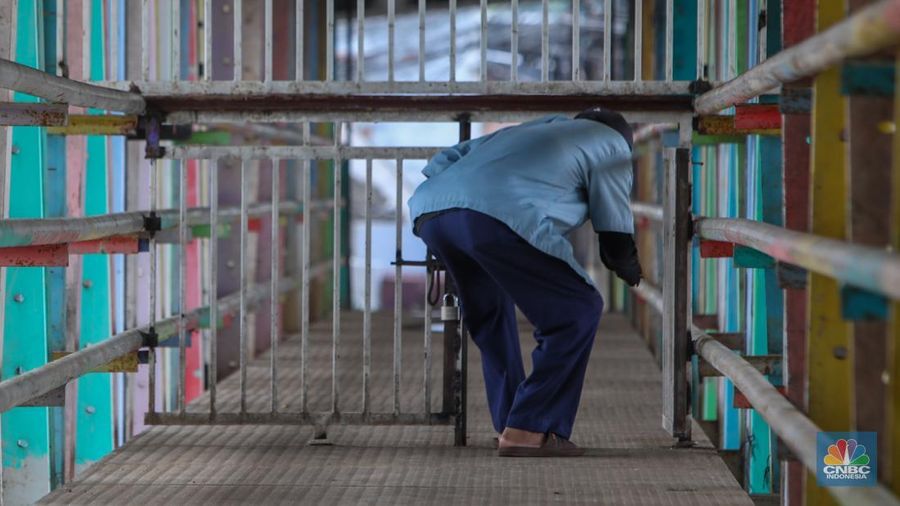 Warga melewati pintu kecil pada gerbang yang menutup akses jembatan penyeberangan orang (JPO) di kolong flyover Kalibata, Jakarta, Rabu (19/2/2025). (CNBC Indonesia/Martyasari Rizky)