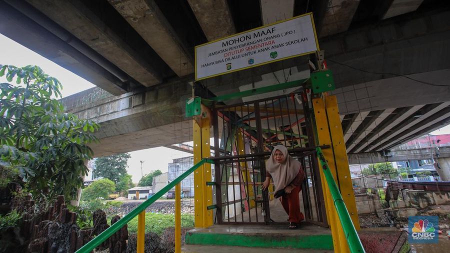 Warga melewati pintu kecil pada gerbang yang menutup akses jembatan penyeberangan orang (JPO) di kolong flyover Kalibata, Jakarta, Rabu (19/2/2025). (CNBC Indonesia/Martyasari Rizky)